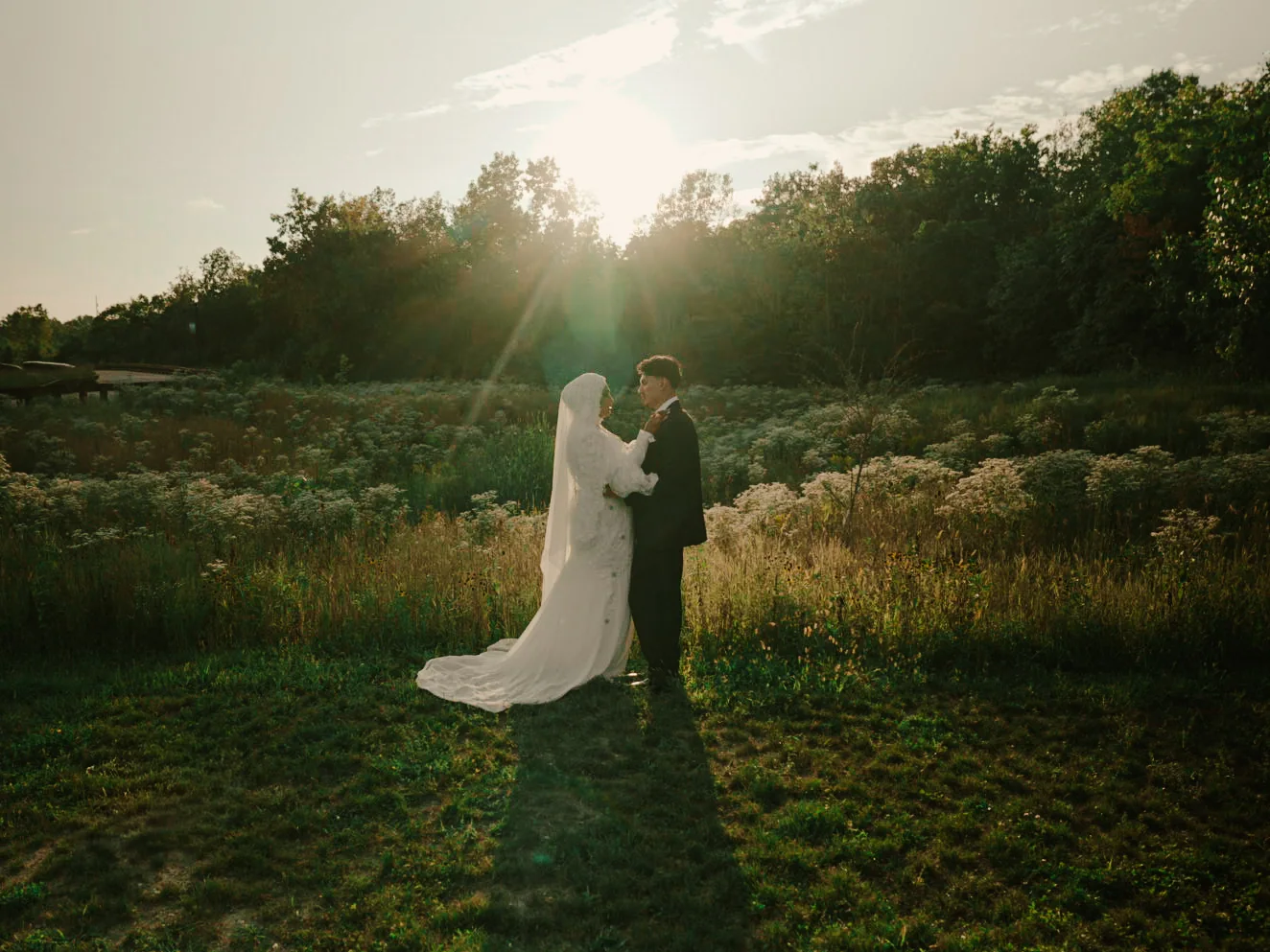 A newlywed couple standing together in a sunlit field
